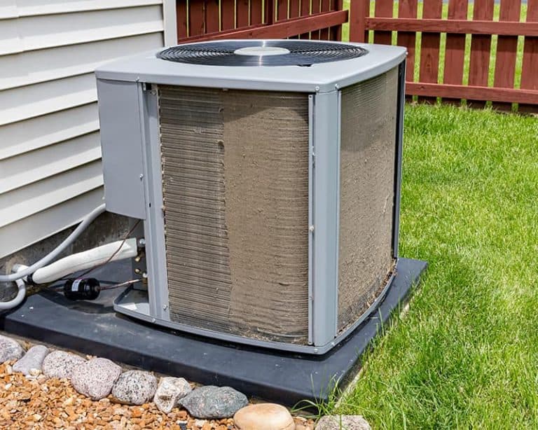 a dirty and blocked outdoor air conditioning unit surrounded by debris and leaves, causing reduced efficiency, increased wear and tear, and higher repair costs.